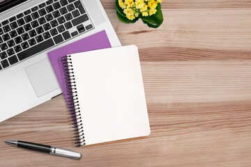 Blank notebook with pen on an office desk table with laptop computer, and supplies.
