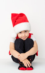 Portrait of sitting happy smiling child in red Santa Claus hat isolated on white background. Beautiful five-year European boy. Banner. Copy space. Merry Christmas mockup design. New Year holiday card
