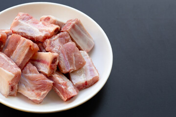 Raw pork ribs in white plate on dark background