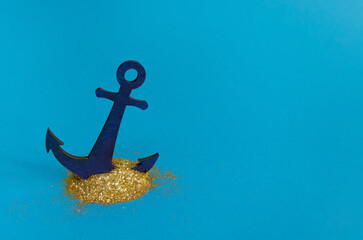 An anchor driven into a shiny gold powder. Feel gold on minimal creative blue background. Top view...