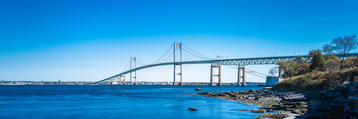 Tranquil seascape with the view of Claiborne Pell Newport Bridge on Route 138 in Rhode Island. Smooth water flows under the bridge, long exposure photography.