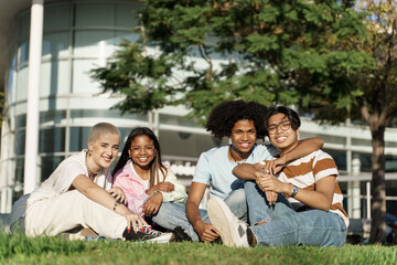 Group portrait of young diverse university college student friends sitting on grass in the campus park