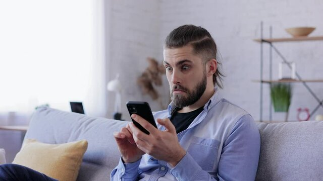 Happy young man surprised by the good shocking and unbelievable news, making yes gesture while looking at smartphone. Enjoying success, celebrating victory, win the lottery, make good deal, get profit
