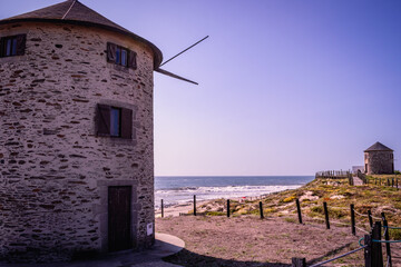 Two windmills on the dunes of Apúlia beach with a wooden fence and cordon delineating the walkway,...