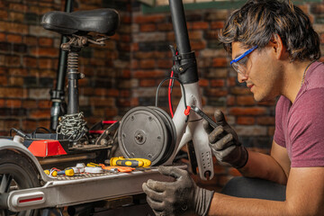 A mechanic sitting using his cell phone while repair an electric scooter in his workshop - obrazy, fototapety, plakaty