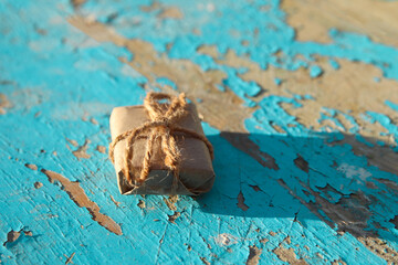 Wrapped vintage gift box with rustic rope bow on blue (turquoise) old wooden background. Present box in craft paper with green bow with shadow. Holiday concept. Close-up. Side view. Art tint