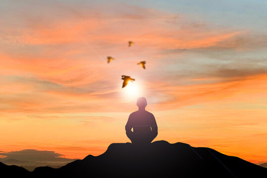 Silhouette of young female sitting practices yoga and meditating in lotus position alone on top of the mountain with beautiful sky and sunrise at the morning with bird on sky. She felt calm and happy.