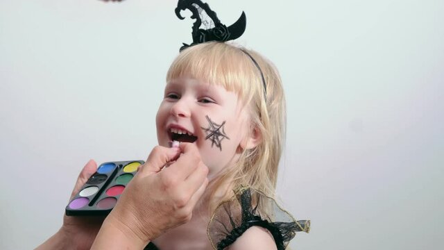 Mother making Halloween makeup on beautiful little blond girl for Halloween party.
