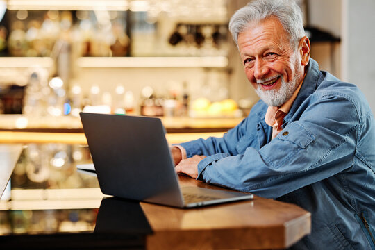 The Happy Senior Student Is Sitting At His Home And Studying For An Exam. Senior Using The Laptop For Studying.