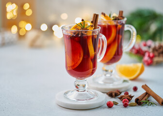 Two glasses of red mulled wine. Hot winter beverage with cinnamon, cardamom, clove, orange, anise, cranberr, fir needles. Selective focus, light blurred background, bokeh, horizontal, copy space