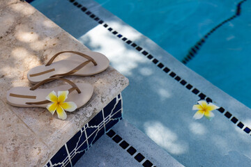 Slippers with frangipani flowers near swimming pool.