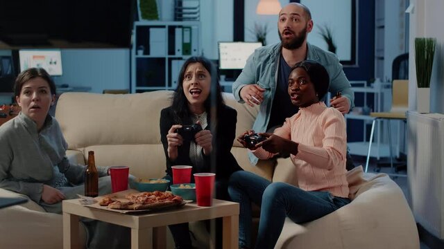 Multi ethnic workmates winning video games on console with controllers after work. Colleagues playing game with joysticks on television to do fun activity and entertainment after hours.