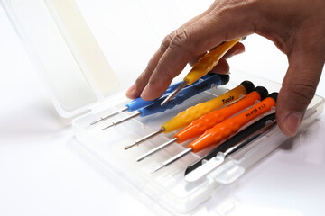 Kit of colored screwdrivers in case on white background. Hand of a person holding a screwdriver. Tool kit for computer and cell phone maintenance