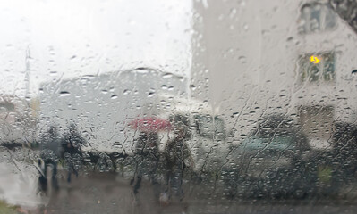 Through the glass with raindrops, the street on which it is raining looks through