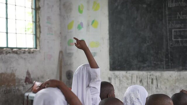 Little muslim African poor school girl with white headscarf raise her hand willing to answer teacher's question in class. Cinematic slow motion shot. Zanz&iacute;bar, Tanzania, Africa 4K.
