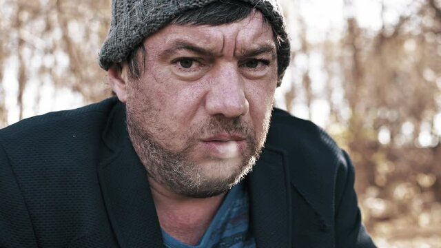 video portrait of a homeless hungry unshaven man on the street in a torn suit smoking a cigarette an old beggar wants to eat looks into the camera close-up.