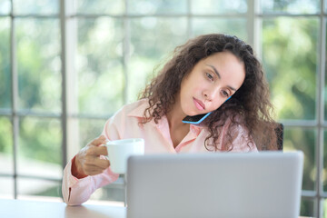 Latino businesswoman using smartphone to talk to customers in office.