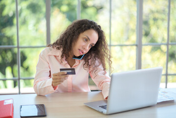 Fototapeta premium A young Latino woman sits at home with a credit card for online shopping with a computer.