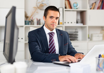 Naklejka premium Portrait of confident focused office employee during daily work with laptop and documents