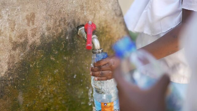 Close up cinematic shot of African black children filling water plastic bottles in a fountain. Water and resource scarcity in Africa 4K.