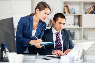 Confident businessman and female colleague working with papers and laptop in modern office