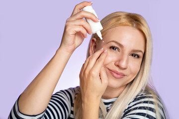 Beautiful Caucasian blonde woman applying eye drops while looking at camera. Eye care concept 