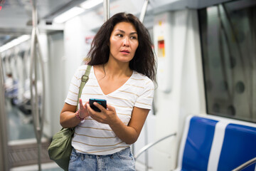 Asian woman with smartphone standing in metropolitan train and waiting for next stop.