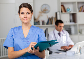 Positive nurse with folder of documents at clinic office