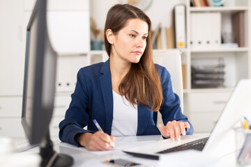 Focused young business woman working alone with laptop and documents in office ..