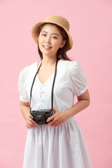 Vertical image of a young woman photographing somebody against a pink background