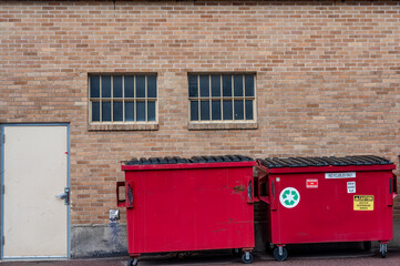 row of covered garbage bins along a brick wall in a back alley