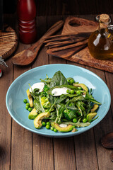 Green healthy spinach salad with avocado and peas on wooden background