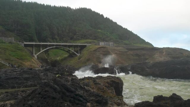 The bridge and shoreline near Thors Well on the Oregon Coast with waves crashing in the rocky inlet on a stormy day.