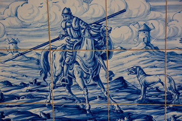 Ritter Don Quijote mit seinem Pferd Rosinante mit Speer kämpfend gegen Windmühlen in La Mancha gemalt auf alten Fliesen  - obrazy, fototapety, plakaty