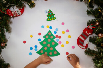 a child girl in a white T-shirt with a New Year's cap on her head cuts a toy original Christmas tree sorter. concept of christmas traditions. development of fine motor skills Montessori at Christmas.