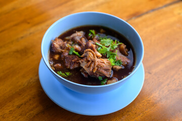 Close up of stewed pork leg with spices in a bowl on rustic table background.