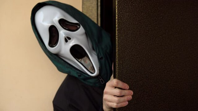A man in a screaming mask appears from the doorway. A maniac in a scary mask is looking at you. Halloween celebration