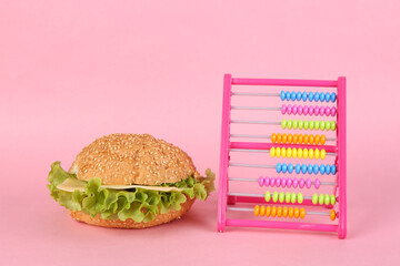 Appetizing burger and abacus on a pink background. Calorie counting, weight loss concept - Powered by Adobe