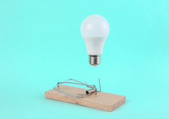 mousetrap with a hovering light bulb on a blue background. Trap, deception, tempting offer concept