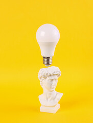Plaster bust of David with floating light bulb on bright yellow background. Minimal idea,...