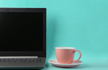 Laptop with a cup of tea or coffee on a blue bright background