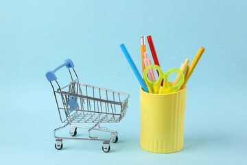 Plastic cup with school stationery, drawing tools and shopping trolley on blue background. Back to school
