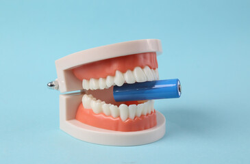 Plastic model of a human jaw with aa battery on blue background. Energy charge