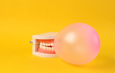 The jaw model inflates a balloon or gum against a bright yellow background. Minimal fun concept