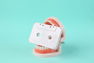 Minimal music concept. Human jaw model with audio cassette in teeth on blue background