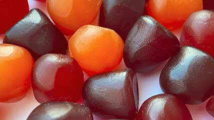 Close-up texture of red, orange and purple multivitamin gummies on white background. Healthy...