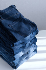 a pile of blue jeans on a light background. Close up. Sunlight. Diagonal
