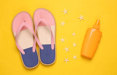 Colored flip flops with sunblock bottle, starfish on yellow background. Beach vacation concept. Flat lay