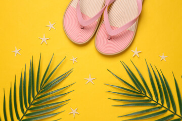 Colored flip flops with green palm leaves, starfish on blue-pink pastel background. Beach vacation,...