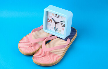 Colored flip flops with clock on blue background. Beach vacation concept.